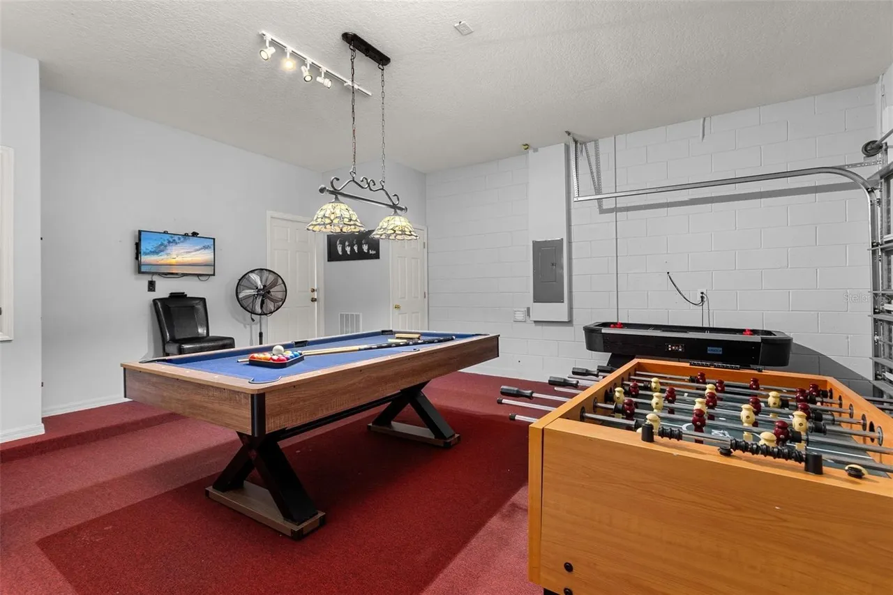 The games room: a blue-felt pool table under stained-glass lamps, a table-football game at the edge of the frame and a leather sofa at the back
